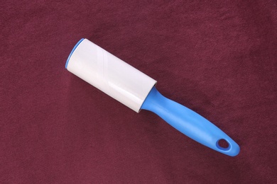 Photo of New lint roller with blue handle on red fabric, top view