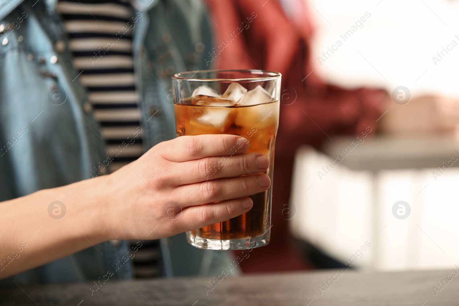 Photo of Woman holding glass of cola with ice at table, closeup. Space for text