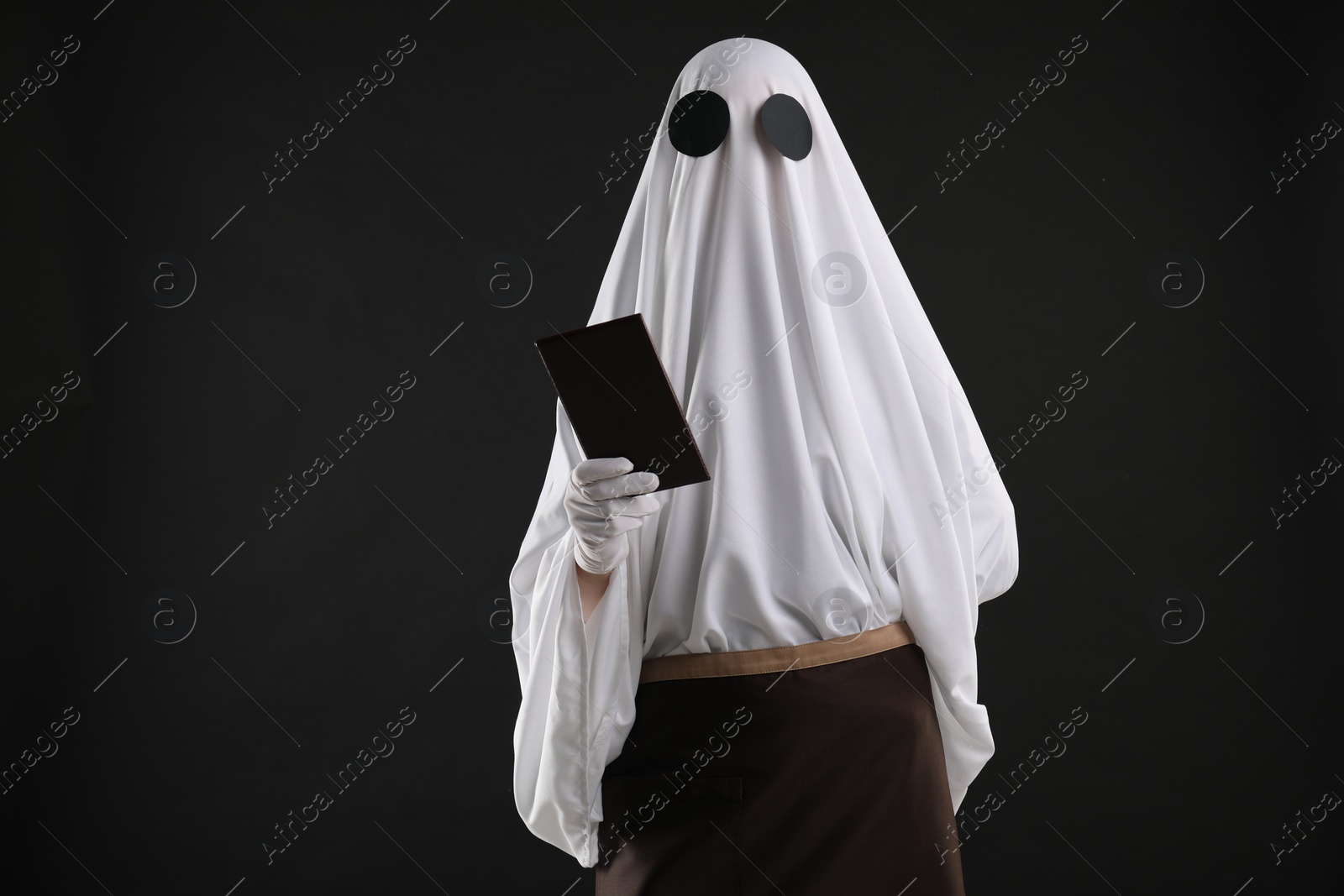 Photo of Creepy ghost. Waiter in white sheet and apron with receipt on black background, space for text