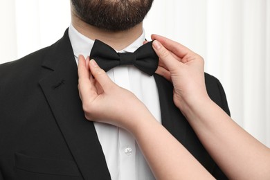 Photo of Woman adjusting bow tie to man indoors, closeup