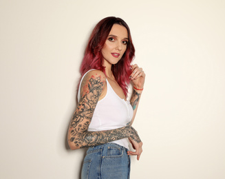 Photo of Beautiful woman with tattoos on arms against light background