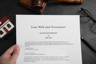 Photo of Woman holding last will and testament at black table, top view