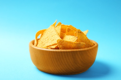 Photo of Tasty mexican nachos chips in wooden bowl on blue background