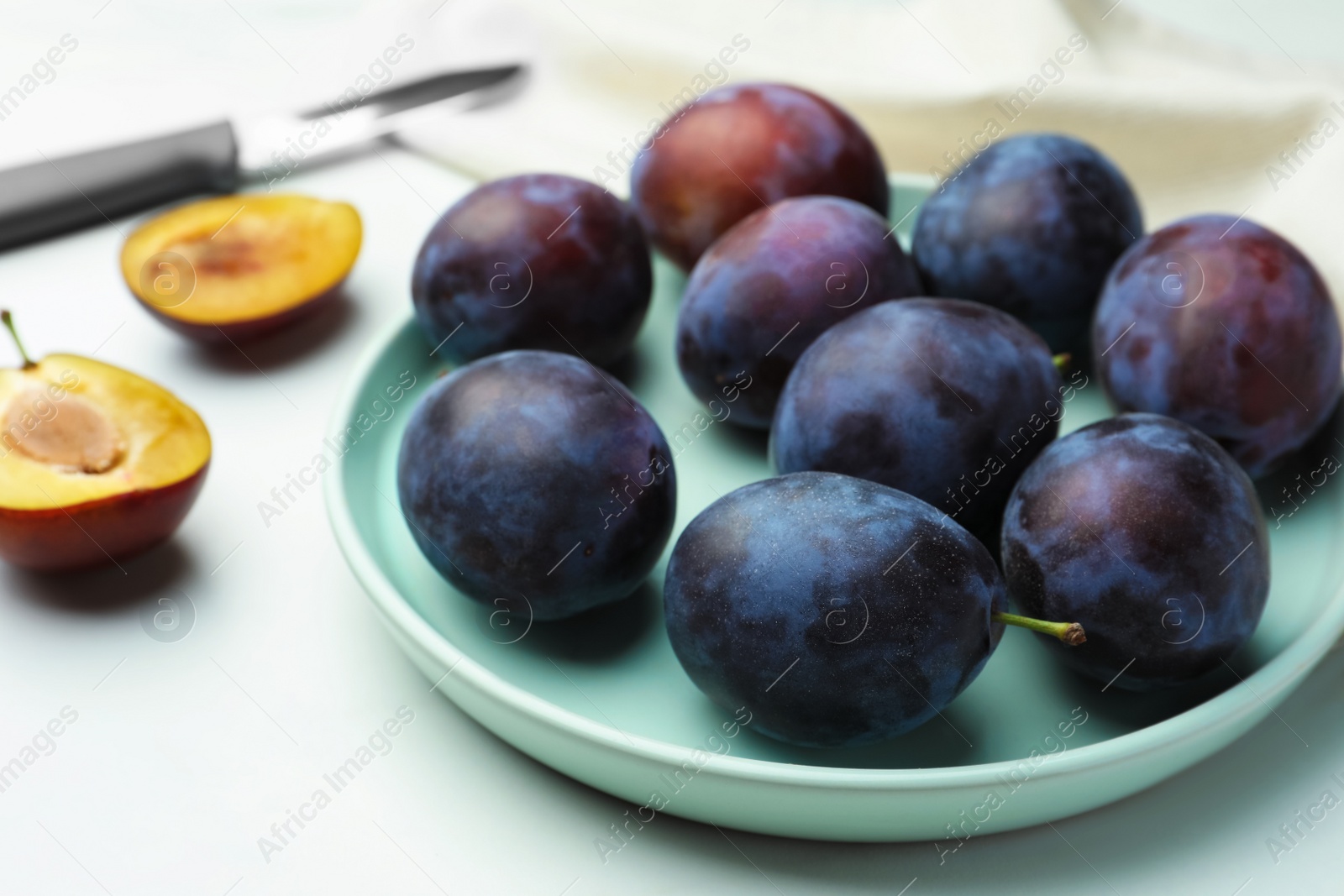 Photo of Plate with tasty ripe plums on white table, closeup