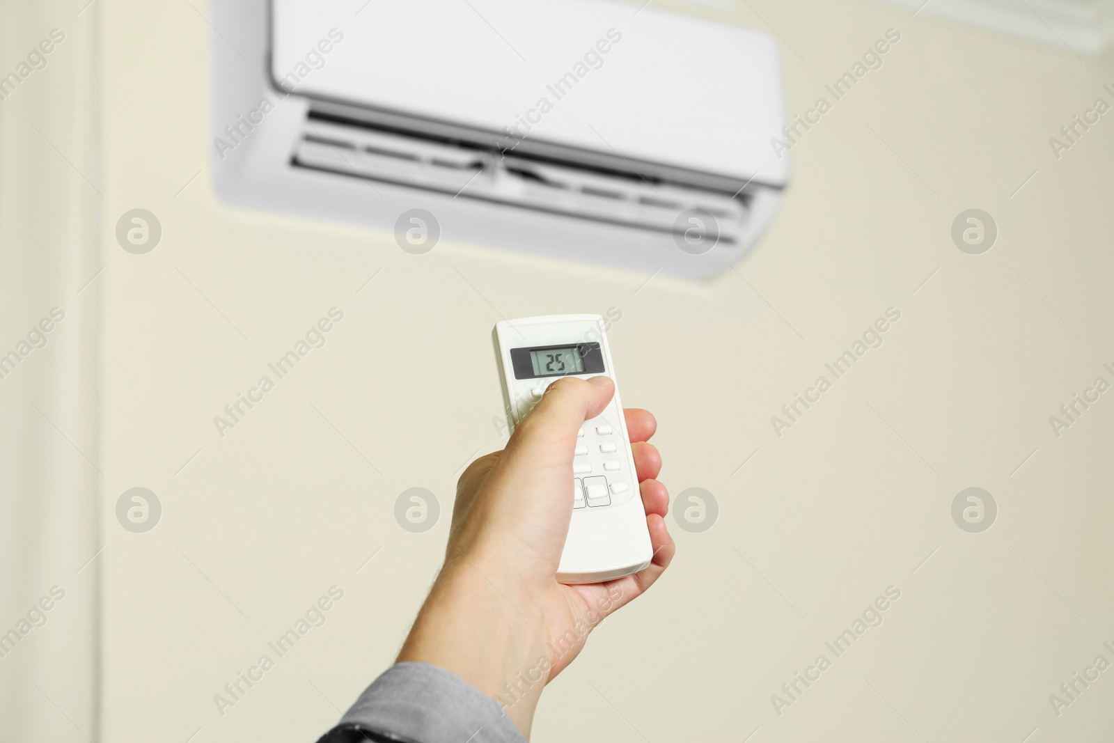 Photo of Man operating air conditioner with remote control indoors, closeup