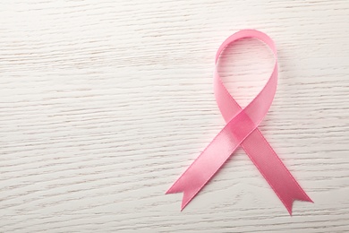 Photo of Pink ribbon on wooden background, top view with space for text. Breast cancer awareness concept