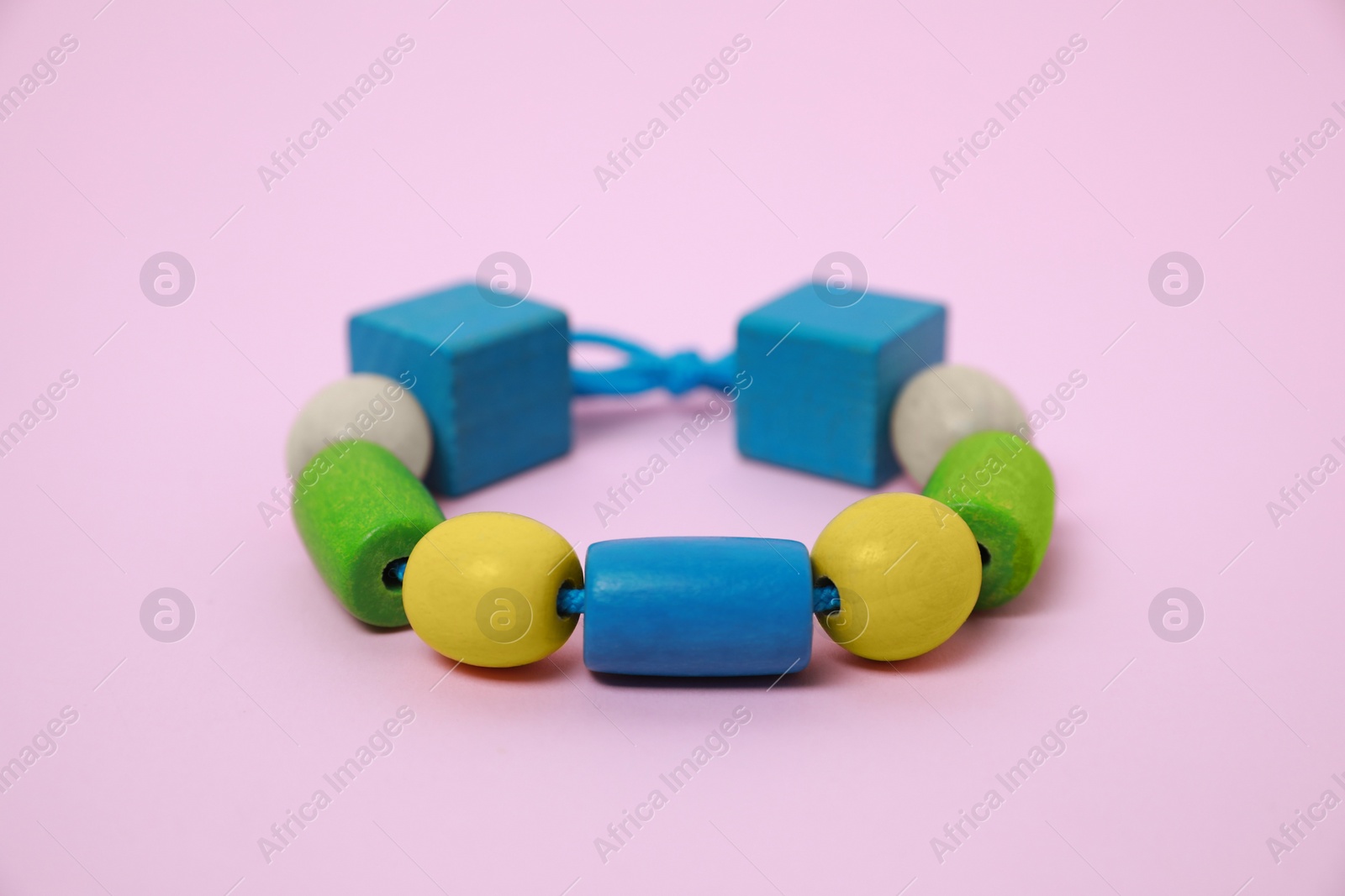 Photo of Wooden pieces and string for threading activity on pink background, closeup. Educational toy for motor skills development