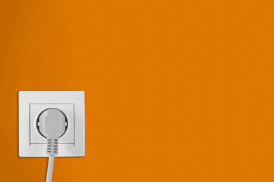Image of Orange wall with power socket and inserted plug, space for text. Electrical supply