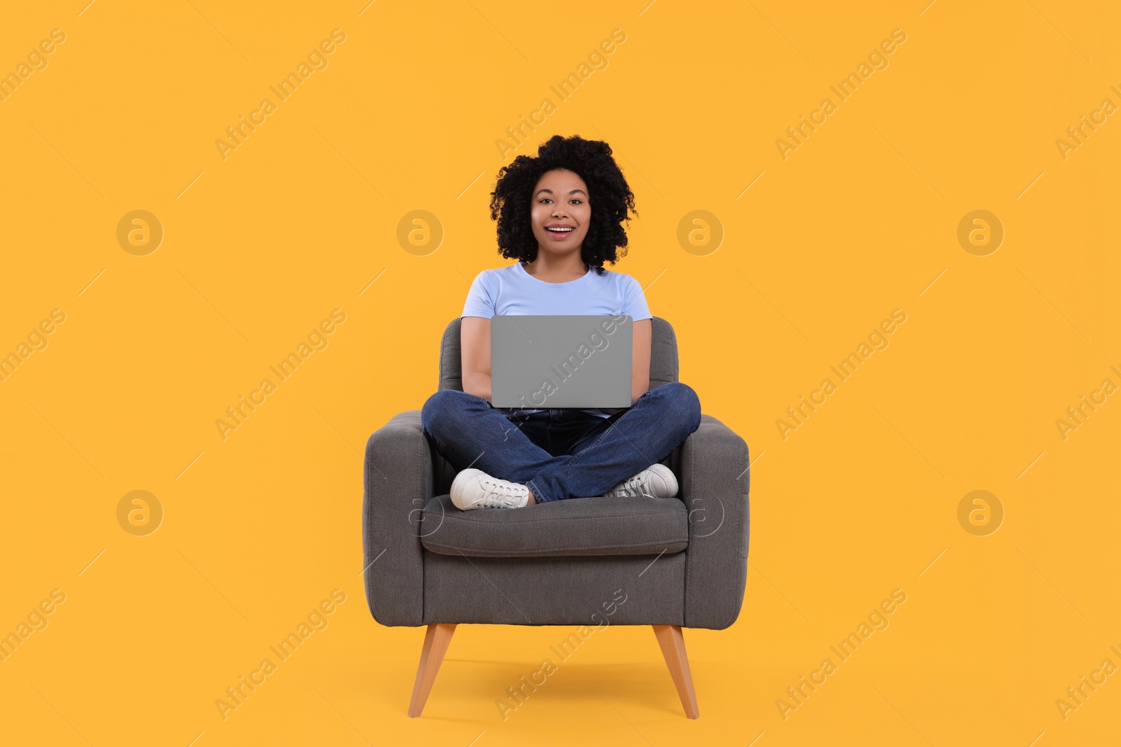 Photo of Happy young woman with laptop sitting in armchair against yellow background