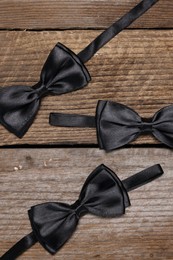 Stylish black bow ties on wooden background, flat lay