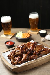 Photo of Tasty chicken wings, sauces, vegetable sticks and glasses of beer on wooden table. Delicious snacks