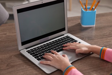 Photo of E-learning. Girl using laptop during online lesson at table indoors, closeup