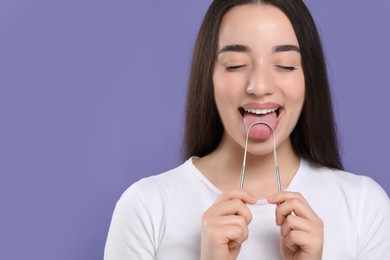 Happy woman brushing her tongue with cleaner on violet background, space for text