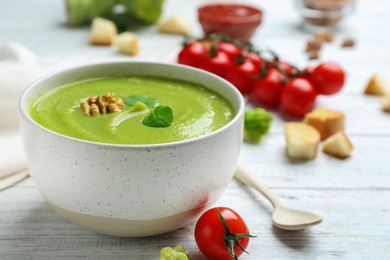 Photo of Bowl of broccoli cream soup with walnut served on white wooden table