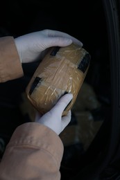 Man with package of narcotics on dark background, closeup