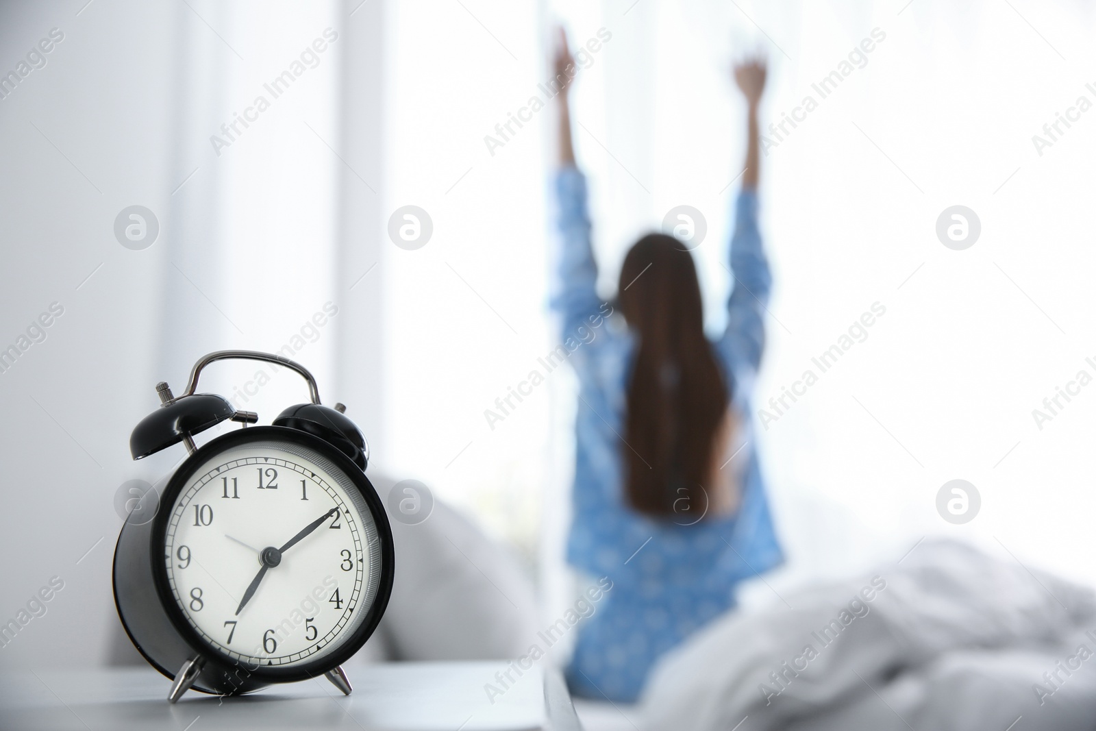 Photo of Young woman stretching at home in morning, focus on alarm clock