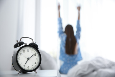 Young woman stretching at home in morning, focus on alarm clock