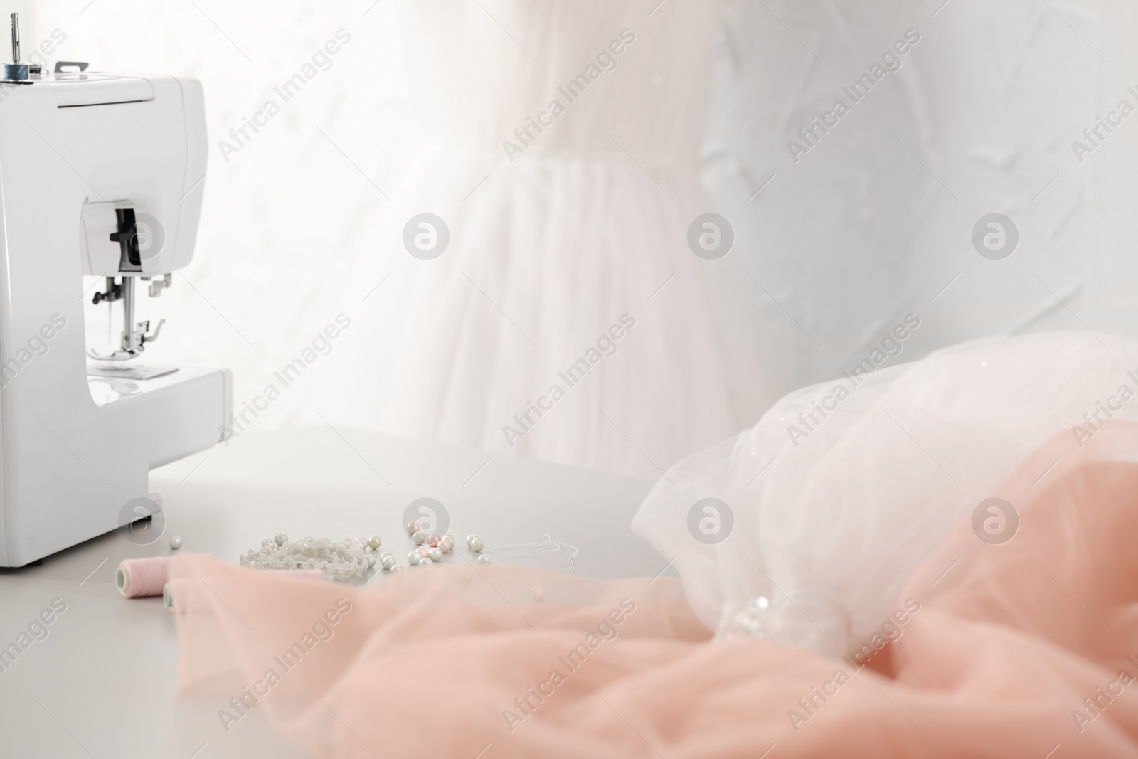 Photo of Sewing machine, fabric, threads and white beads on table in atelier, closeup