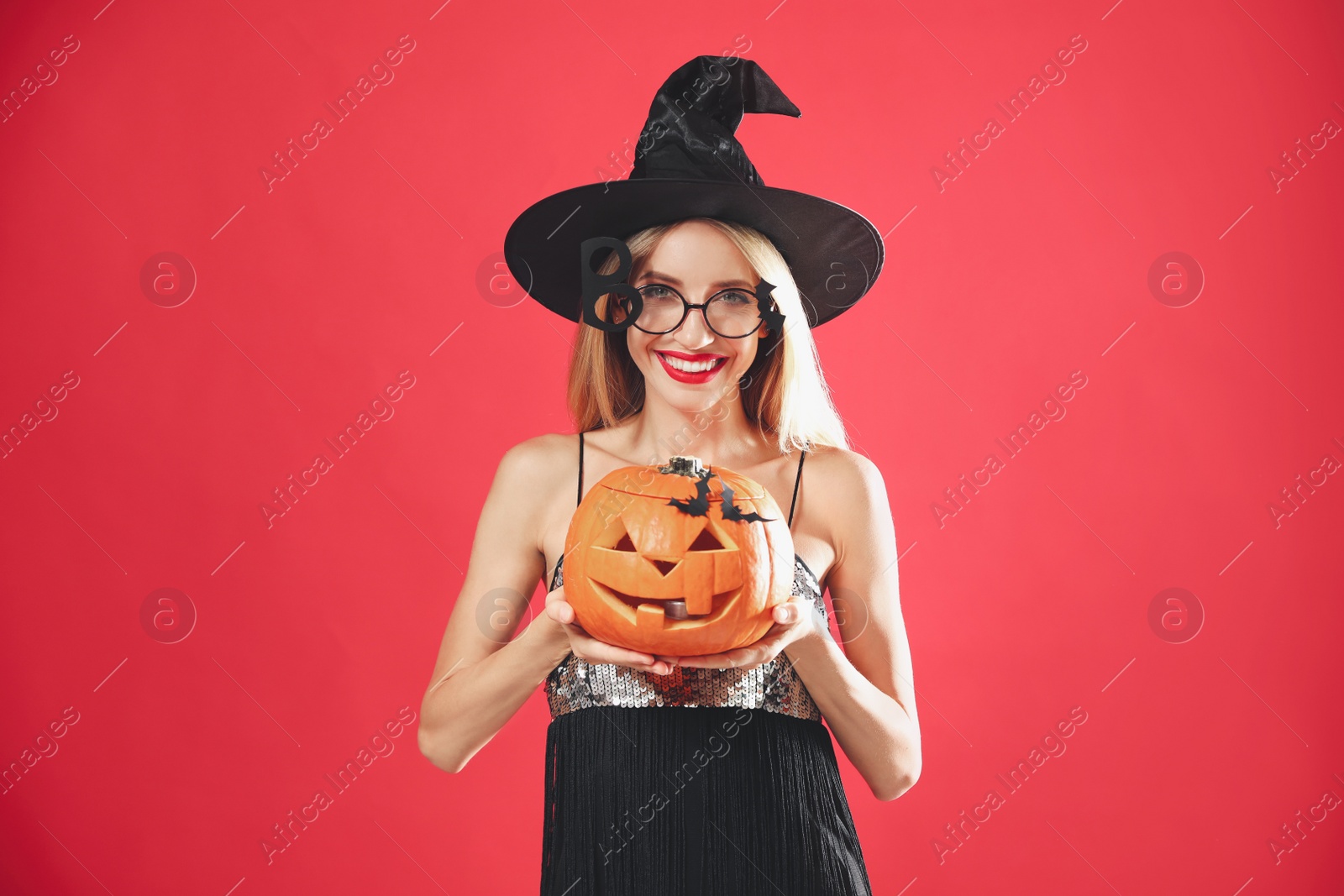 Photo of Beautiful woman in witch costume with jack o'lantern on red background. Halloween party