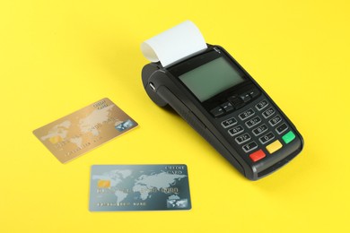 Photo of New modern payment terminal and credit cards on yellow background