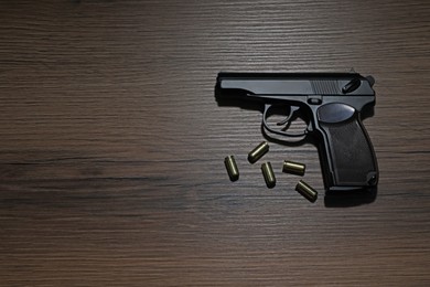 Handgun and bullets on wooden table, flat lay. Space for text