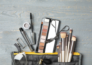 Photo of Cosmetic bag with makeup products and beauty accessories on wooden background, flat lay