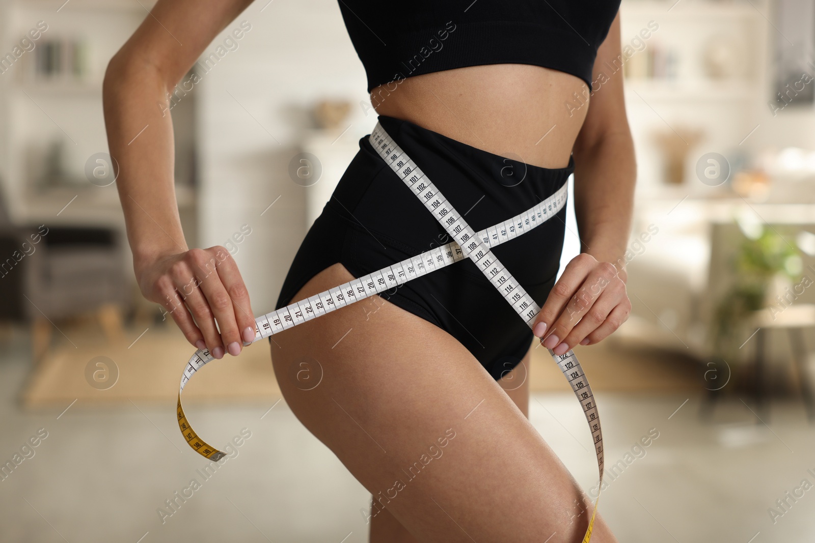 Photo of Young woman measuring waist with tape at home, closeup