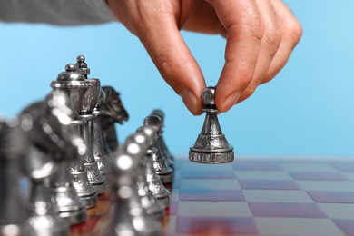 Photo of Man with game piece playing chess over checkerboard against light blue background, closeup
