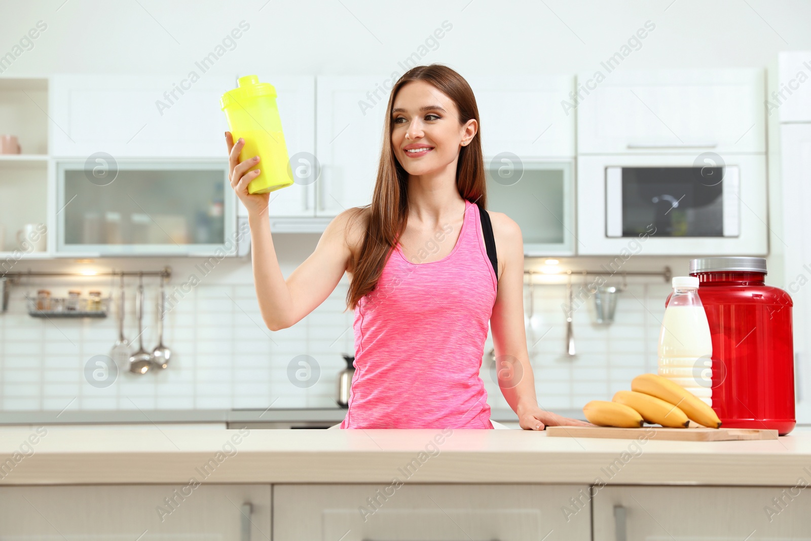 Photo of Young woman with bottle of protein shake in kitchen