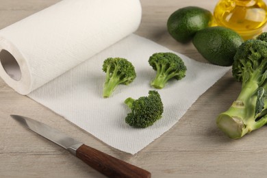 Photo of Paper towels, broccoli, avocados and knife on light wooden table