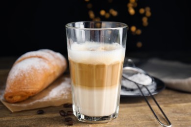 Delicious latte macchiato, croissant and coffee beans on wooden table