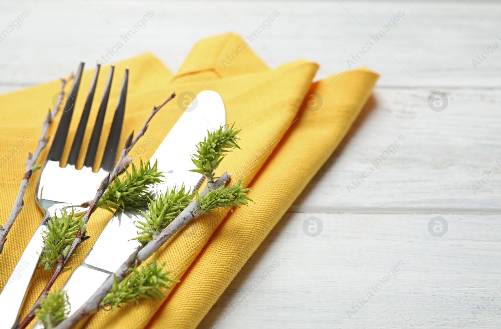 Photo of Cutlery set with beautiful willow branches on white wooden table, closeup. Easter celebration