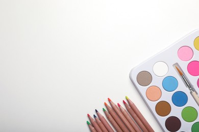 Watercolor palette and colorful pencils on white background, flat lay. Space for text