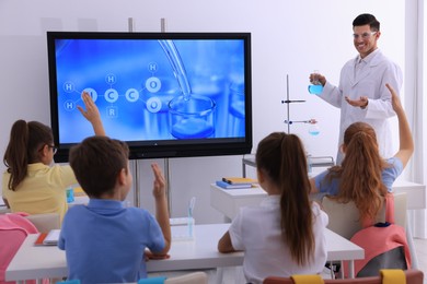 Photo of Teacher holding flask with solution near interactive board in classroom during practical lesson