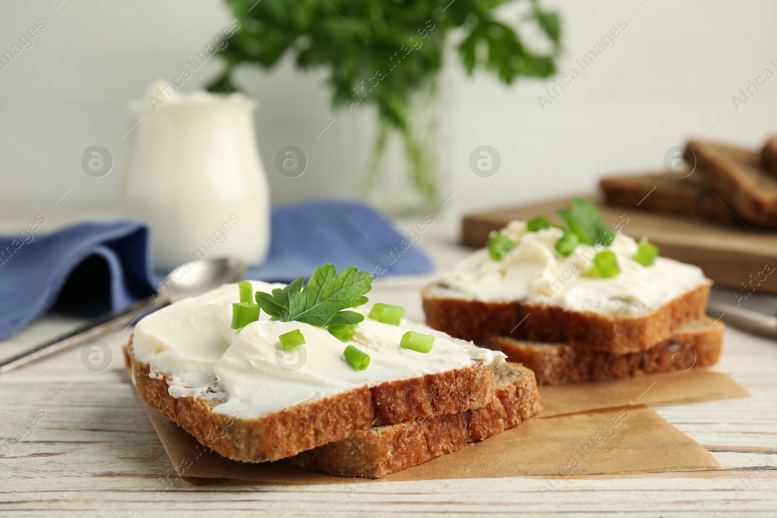 Photo of Bread with cream cheese, green onion and parsley on white wooden table