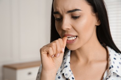 Photo of Young woman biting her nails at home