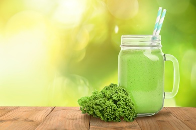Image of Mason jar with fresh kale smoothie on wooden table against blurred background, space for text