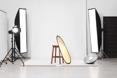 Photo of Stool with light reflector, professional lighting equipment and white background in photo studio