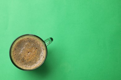 Aromatic coffee in glass cup on green background, top view. Space for text