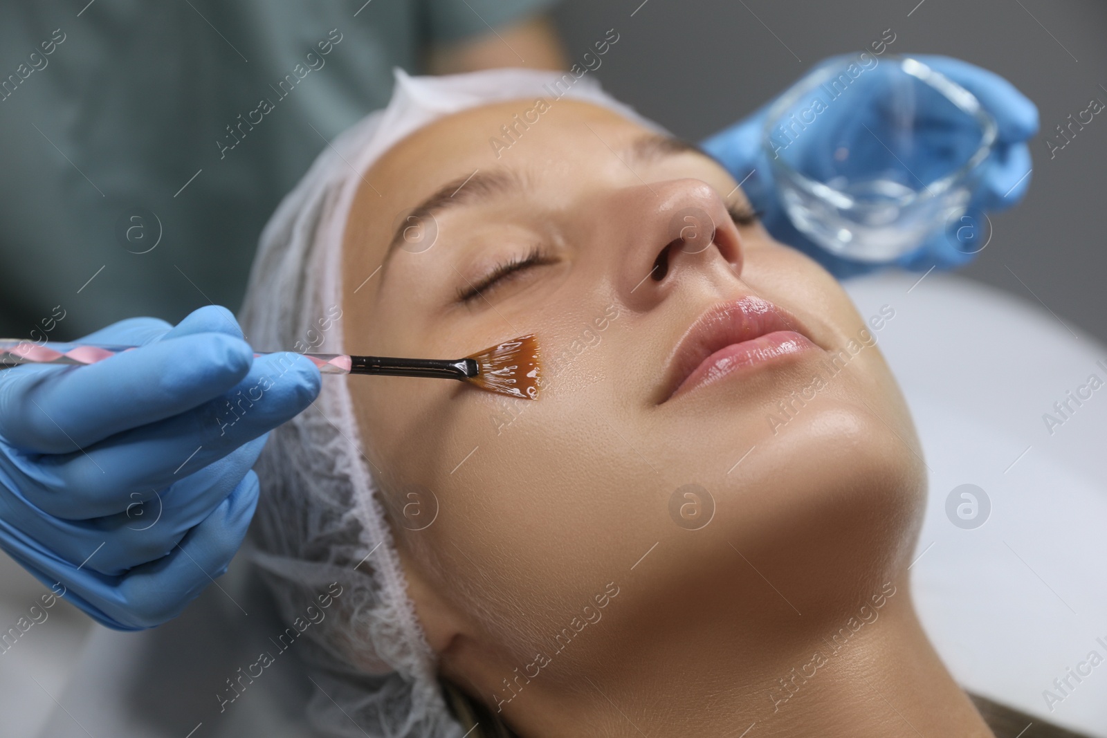 Photo of Cosmetologist applying cosmetic product for chemical peeling on client's face in salon