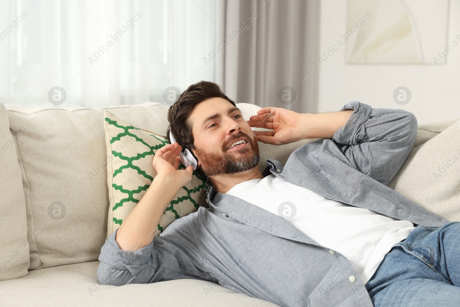 Photo of Happy man listening music with headphones on sofa indoors