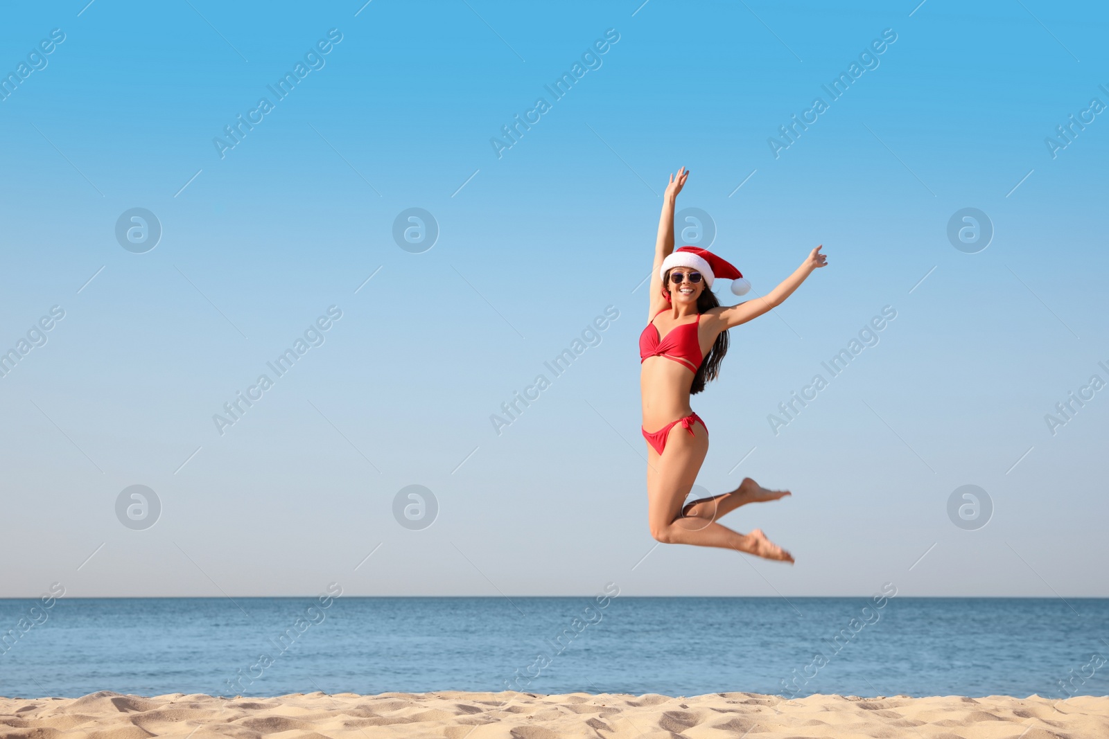 Photo of Beautiful young woman in Santa hat and bikini having fun on beach, space for text. Christmas vacation