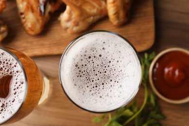 Glasses with beer and delicious baked chicken wings on wooden table, closeup