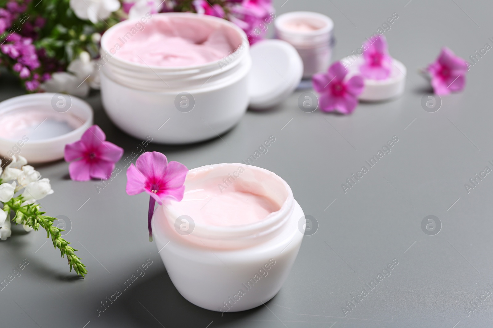 Photo of Jars of body cream and flowers on grey background
