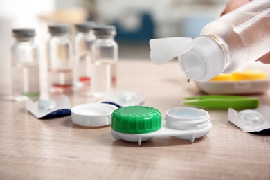 Photo of Woman dripping solution into contact lens case on table, closeup