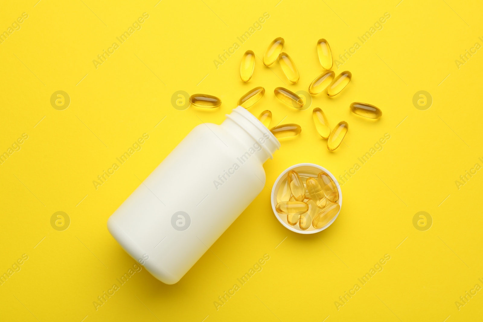 Photo of Softgel capsules, lid and bottle on yellow background, flat lay