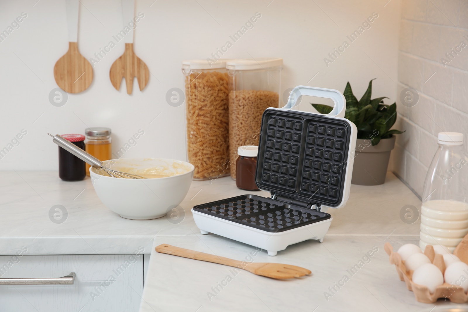 Photo of Modern electric waffle maker and ingredients on white countertop indoors