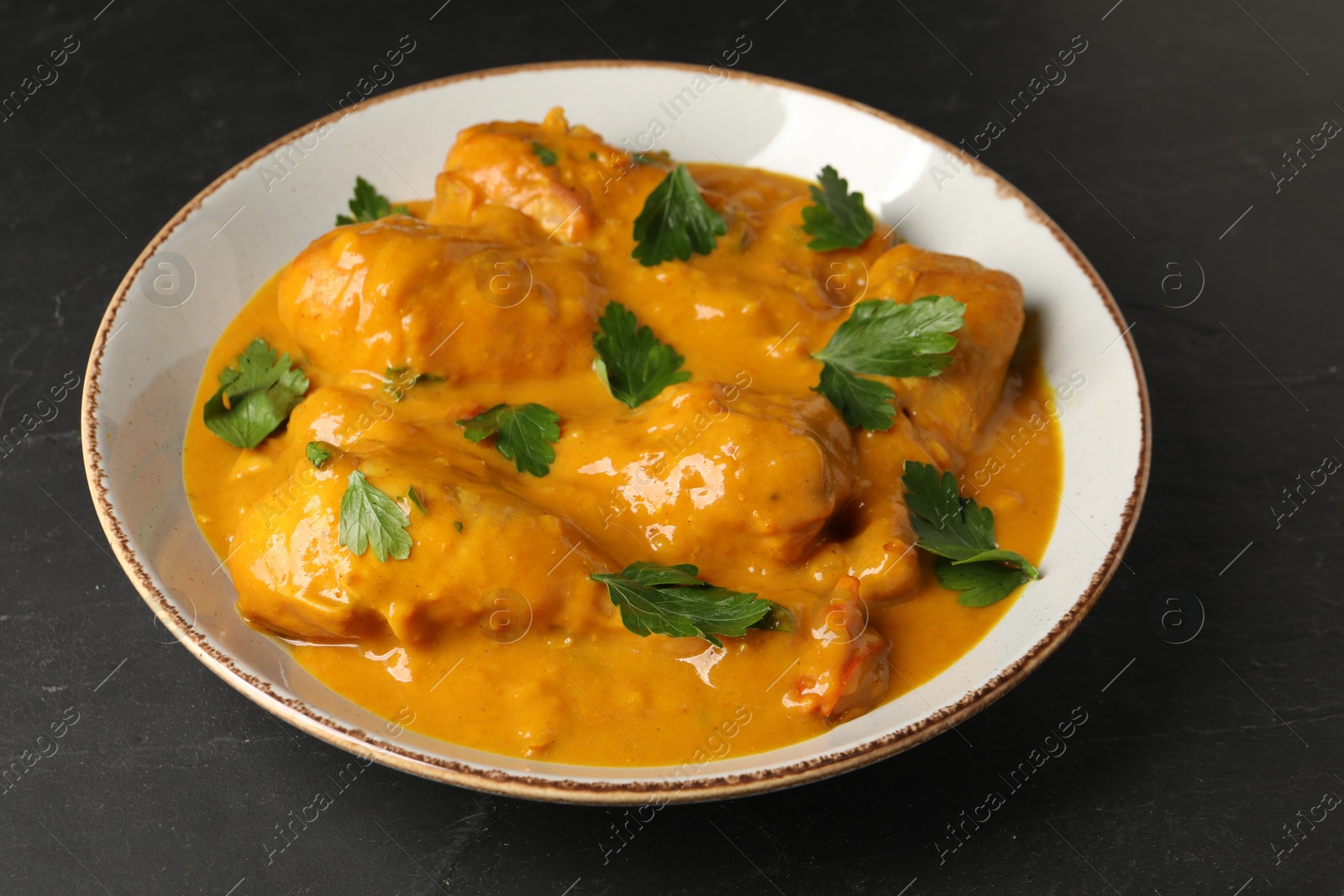 Photo of Tasty chicken curry with parsley on black textured table, closeup