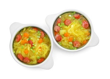 Bowls of delicious sauerkraut soup with smoked sausages and green onion on white background, top view