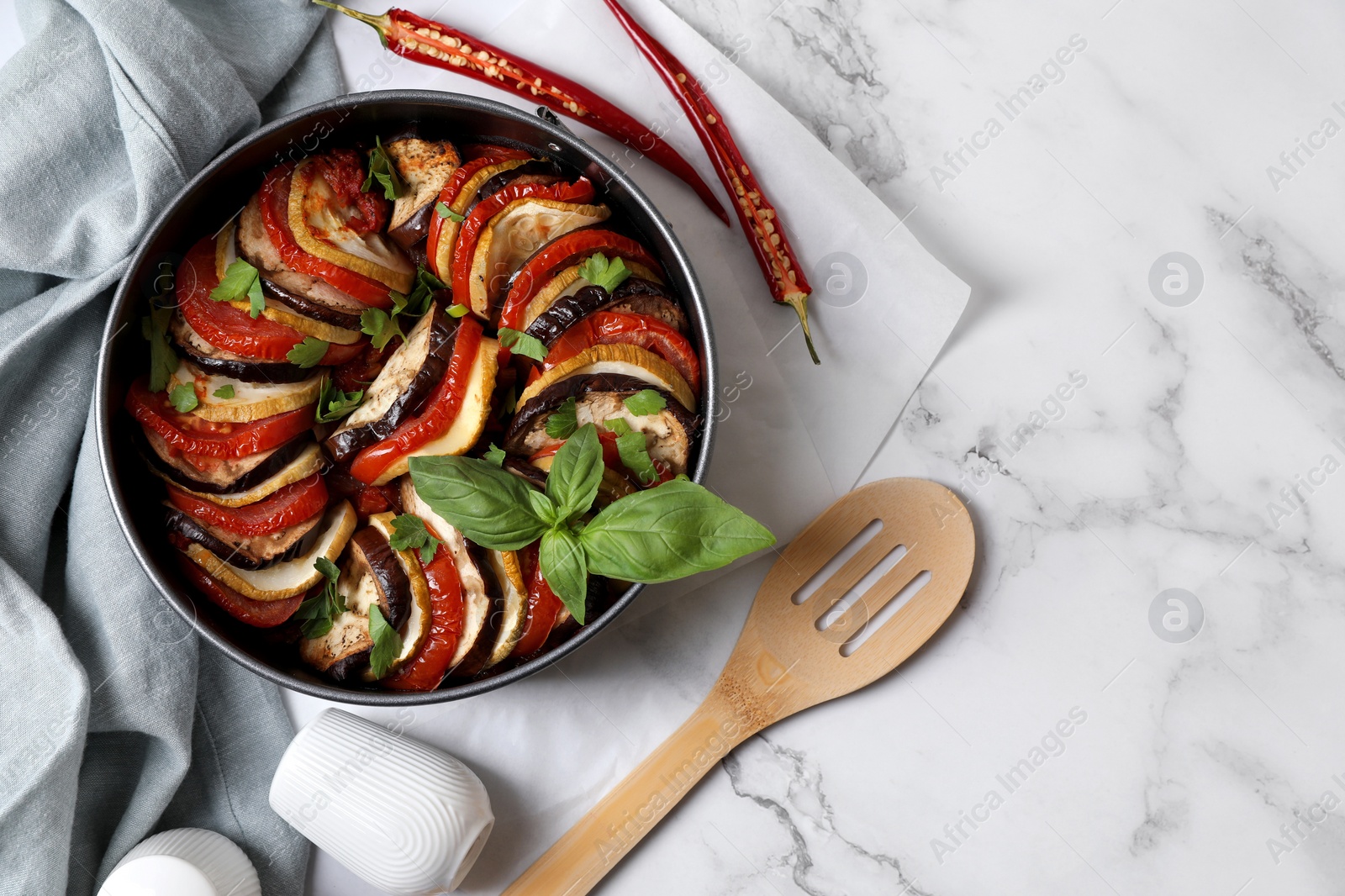 Photo of Delicious ratatouille, chili peppers and spatula on white marble table, flat lay. Space for text